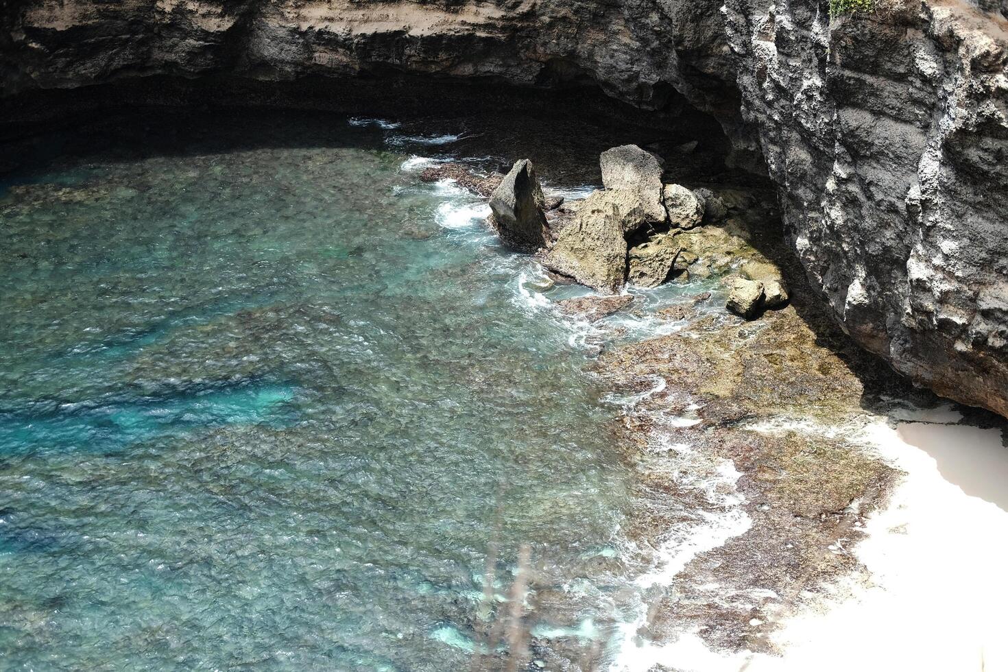Beautiful landscape aerial view of cave on rocky cliff at the sea with foam waves and splash water. Travel destination seascape of summer calm ocean in Bali at Indonesia photo