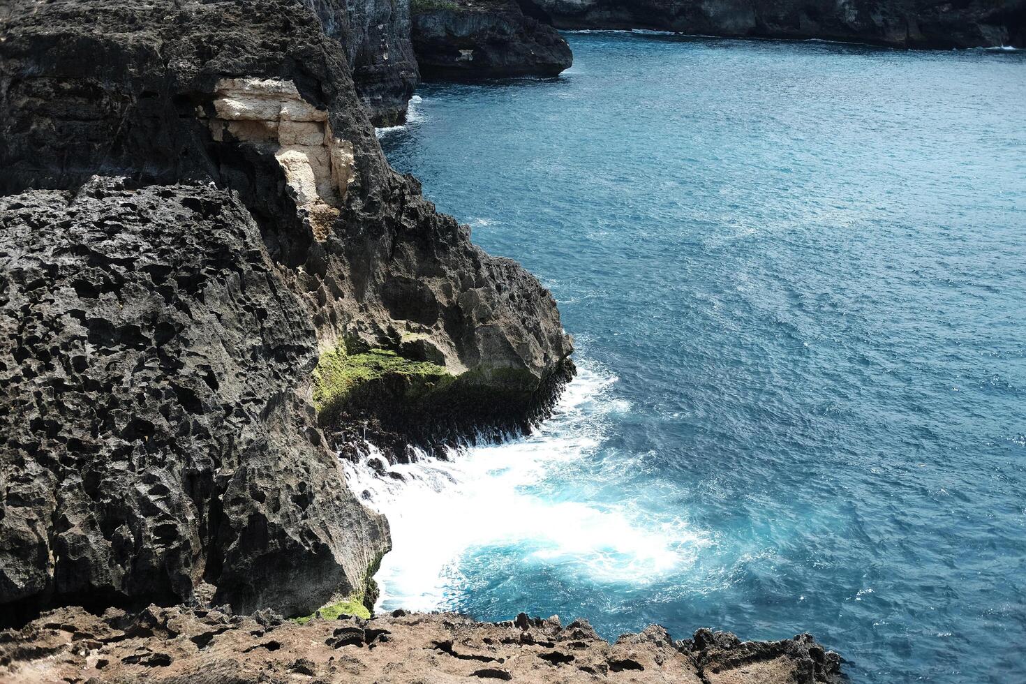 Beautiful landscape aerial view of cave in rocky cliff at the sea with foam waves and splash water. Travel destination seascape of summer calm ocean in Bali at Indonesia photo