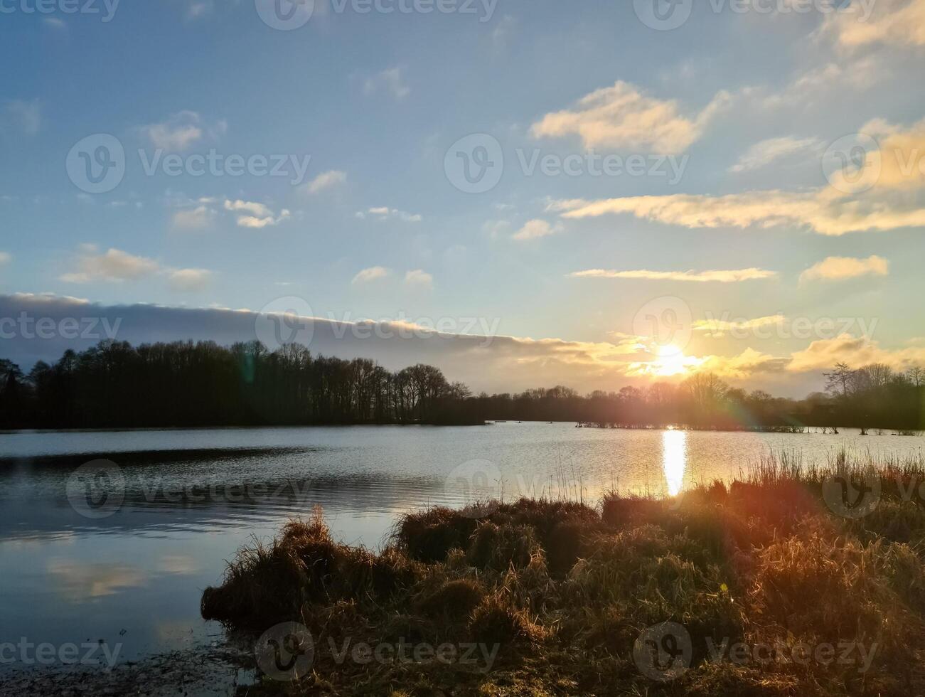 Sunset reflecting on calm lake with cloudy sky and trees silhouette photo