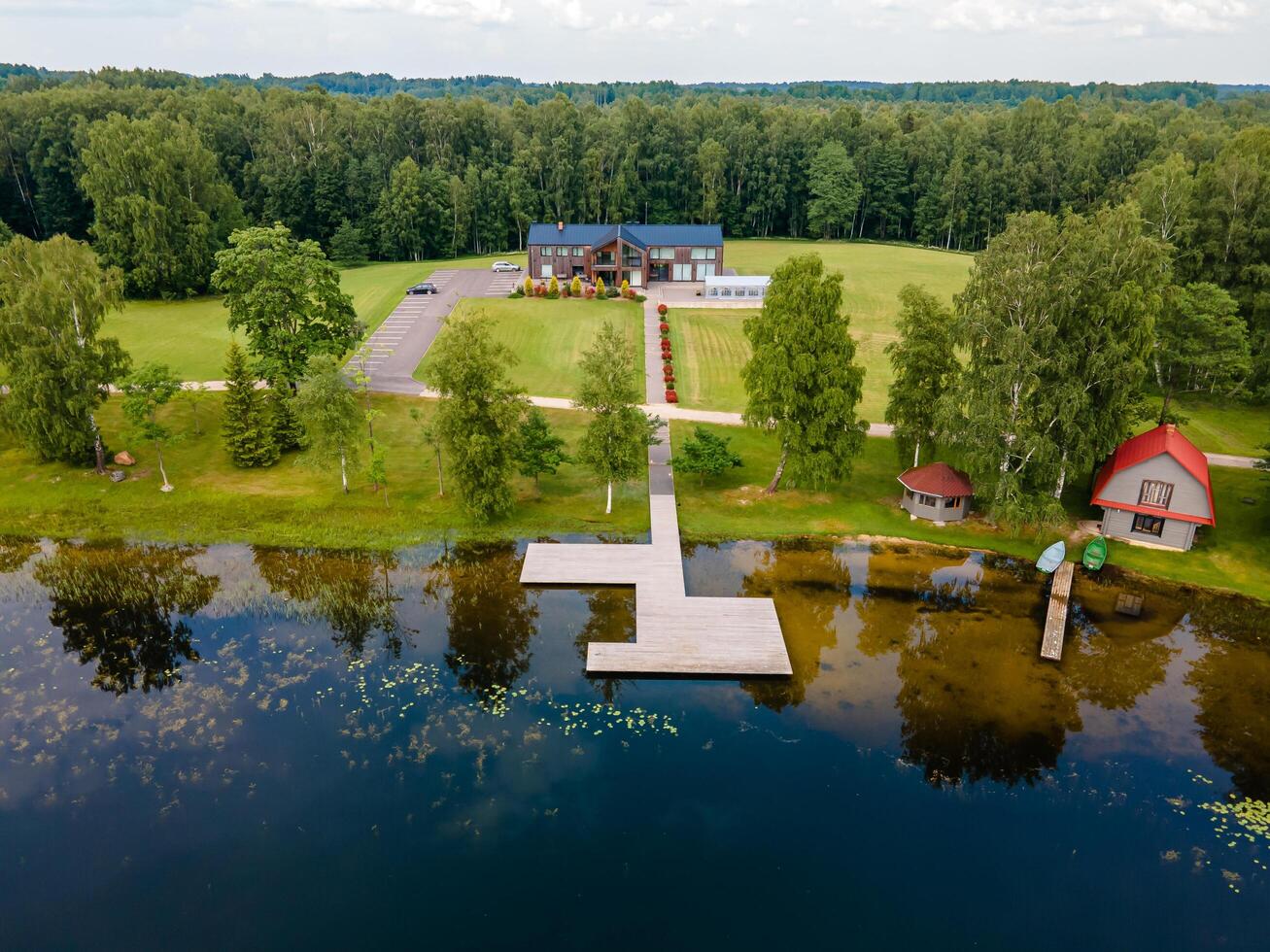 Riga, Latvia, 2024 - Lakeside View with Wooden Dock and Modern House in Forested Area photo