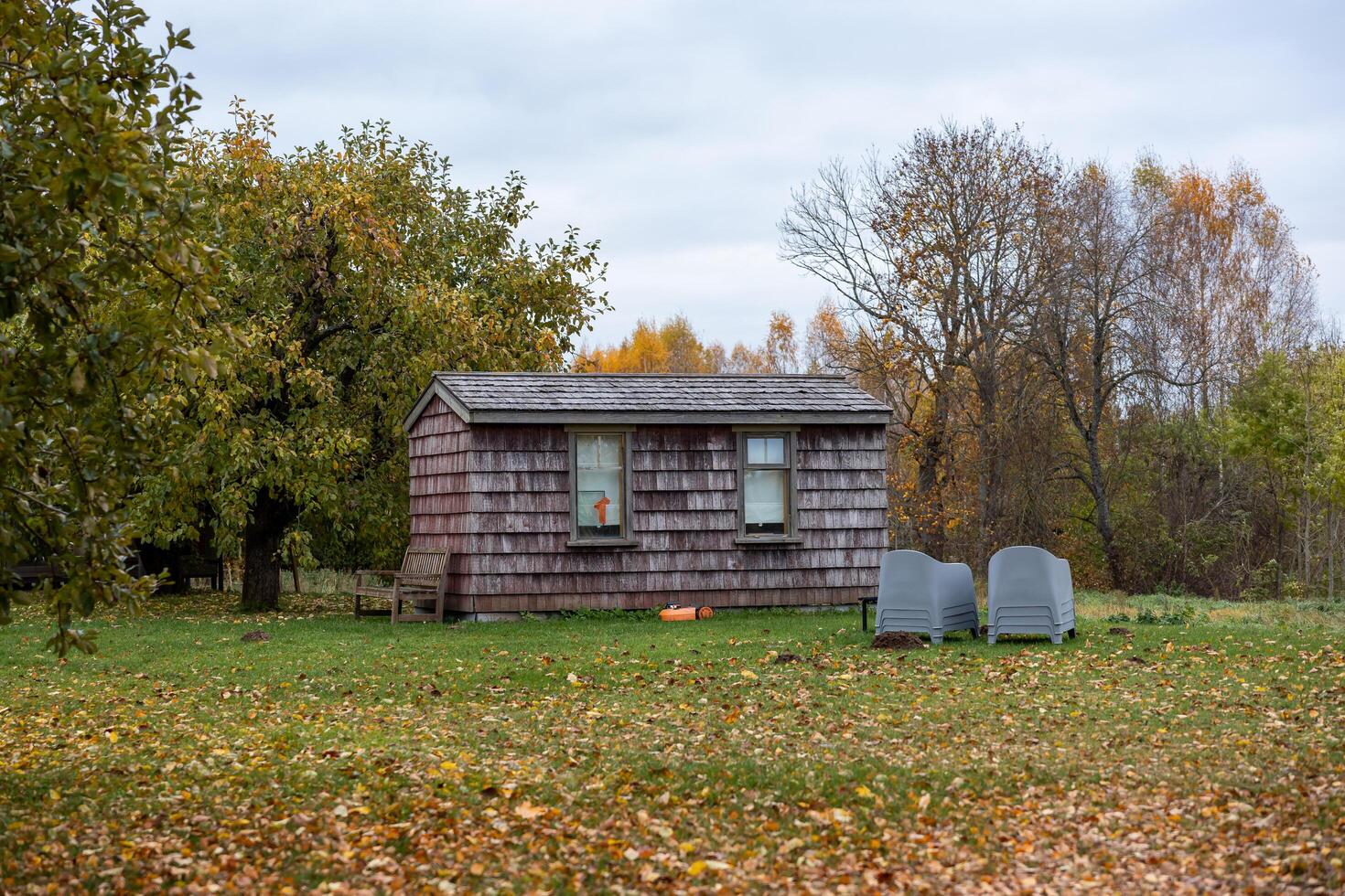 Riga, Latvia, 2024 - Wooden Cabin with Autumn Foliage and Gray Chairs in Grassy Area photo