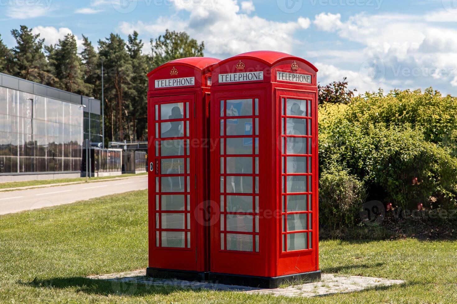 Red British Telephone Boxes with Modern Building and Trees photo