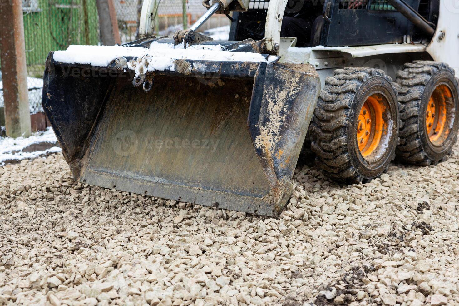 Skid Steer Loader with Orange Wheels Working on Crushed Stones photo