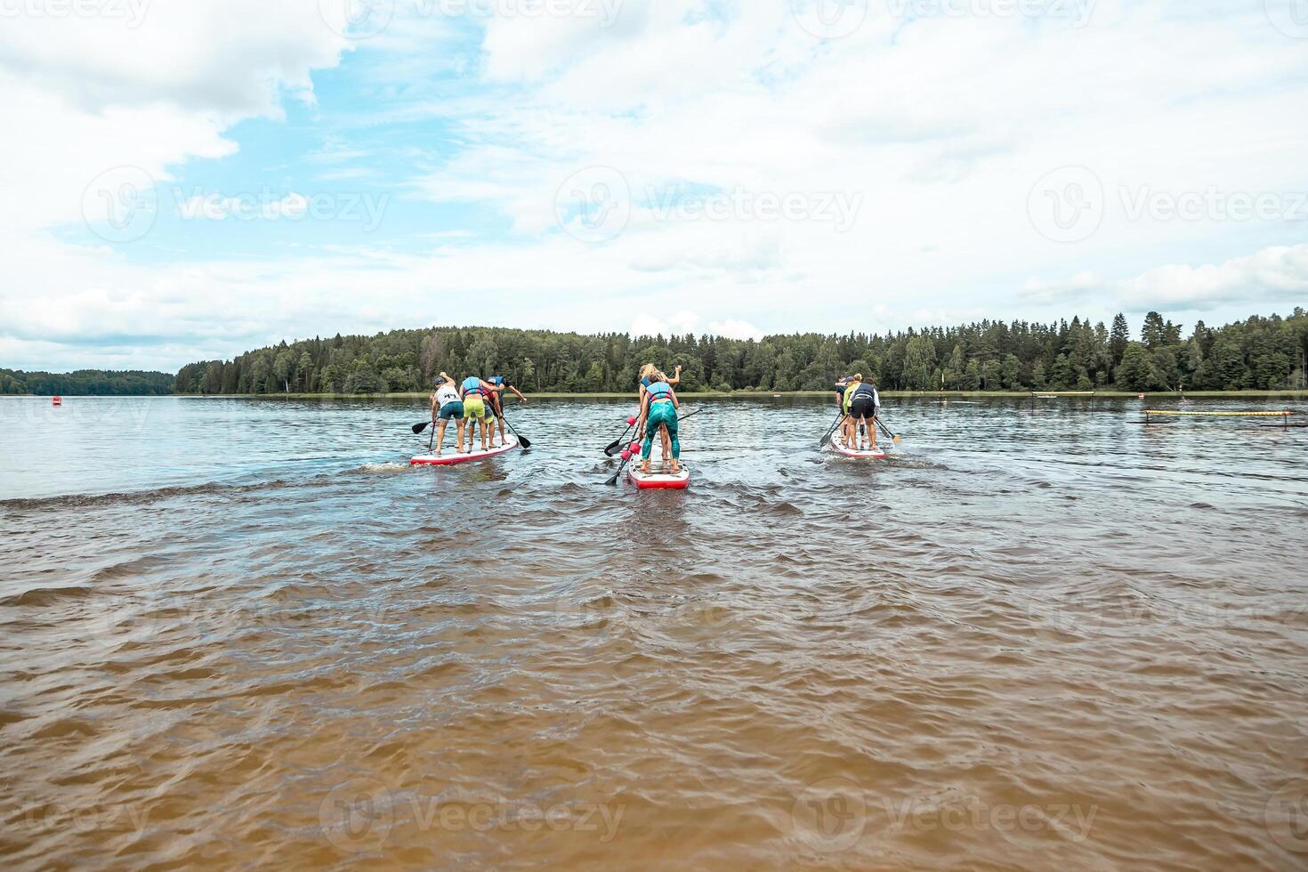 Paddleboarders on a Calm Lake with Forested Shoreline and Clouds photo