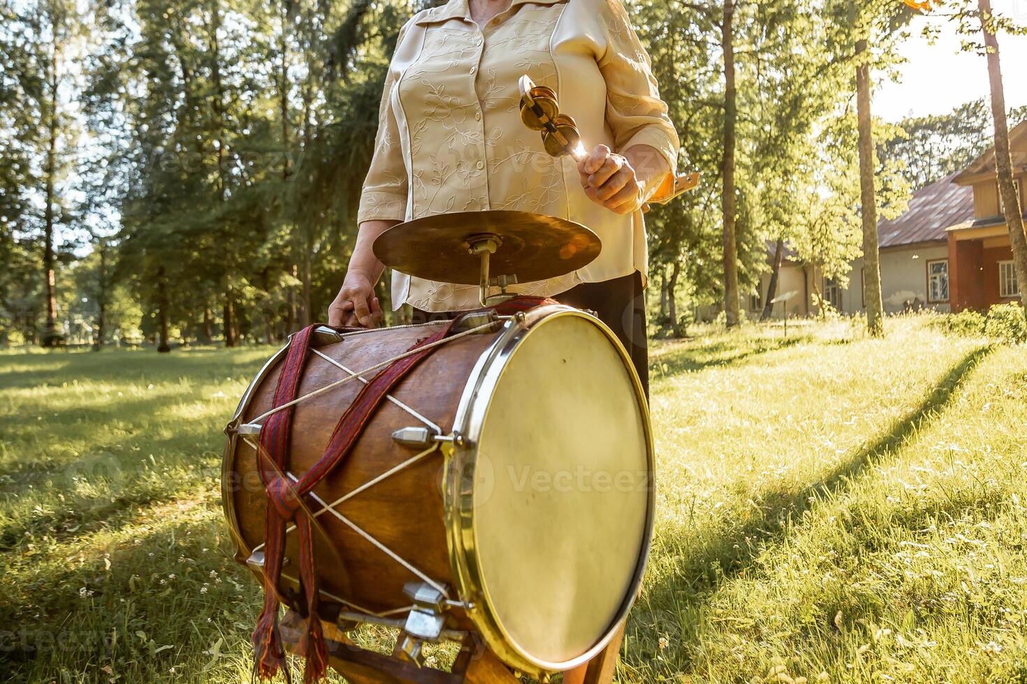 Person Holding Drum and Mallet Outdoors Near Tall Trees and House photo
