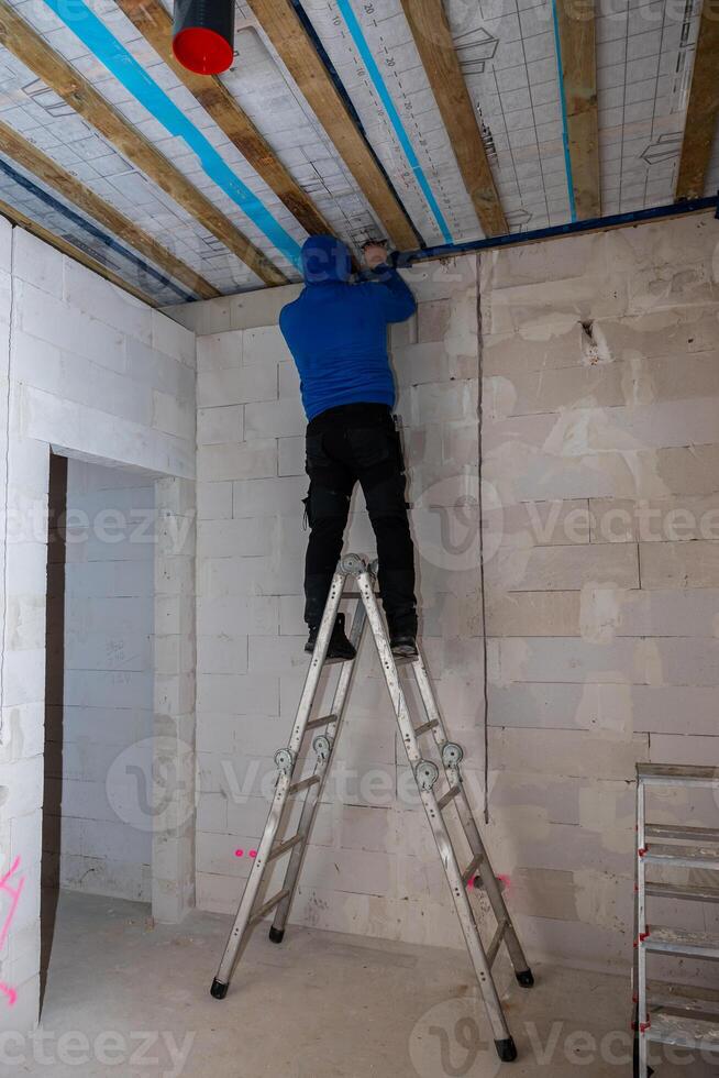 Worker on Ladder Installing Ceiling with Exposed Wooden Beams photo