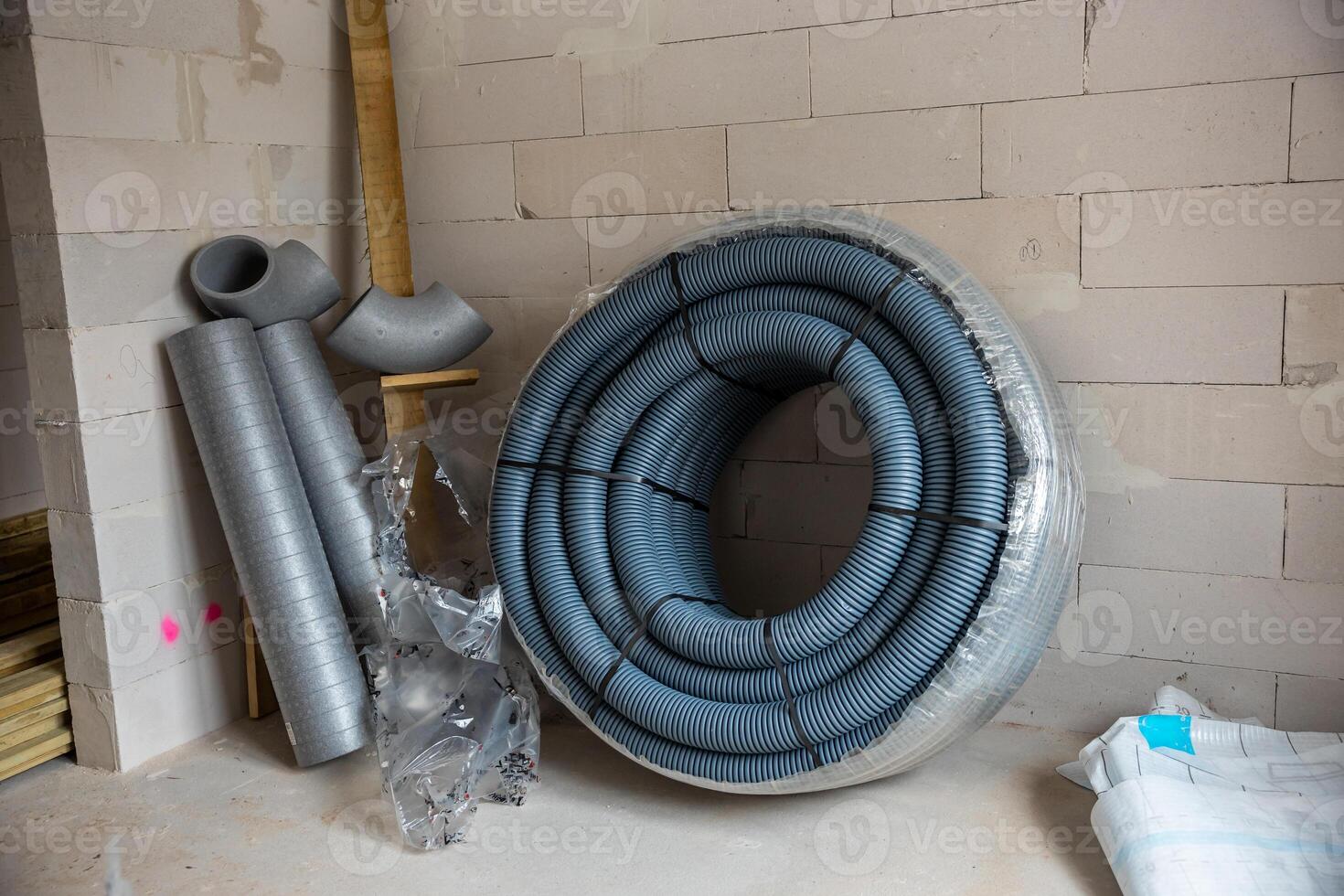 Construction Materials with Coiled Blue Ventilation Duct on Unfinished Floor photo