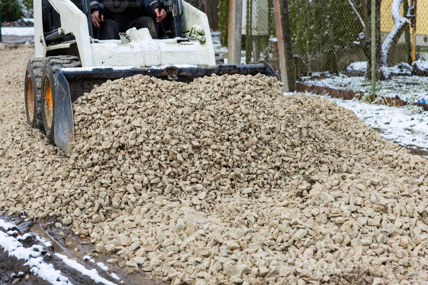 Construction Vehicle Spreading Crushed Stones on Snowy Pathways photo
