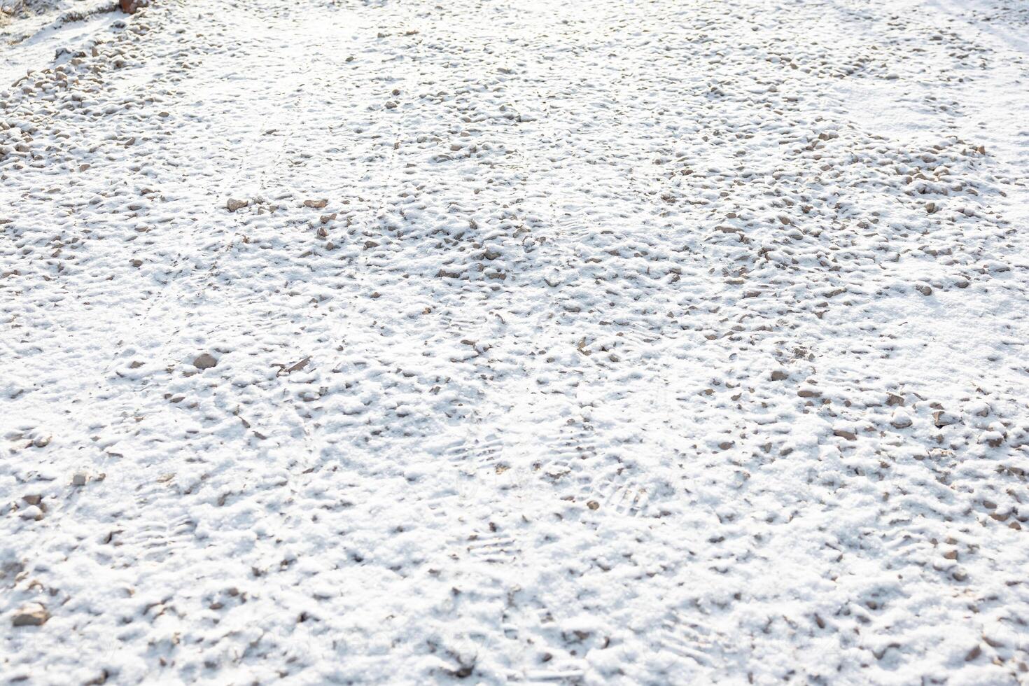 Snow Covered Ground with Footprints and Scattered Pebbles photo