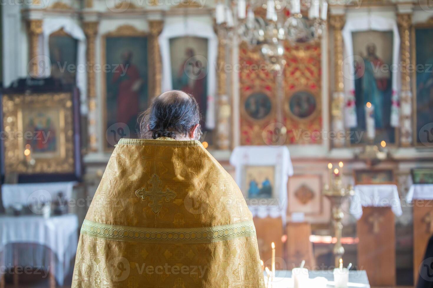Orthodox Priest in Golden Robe Standing Before Ornate Iconostasis photo