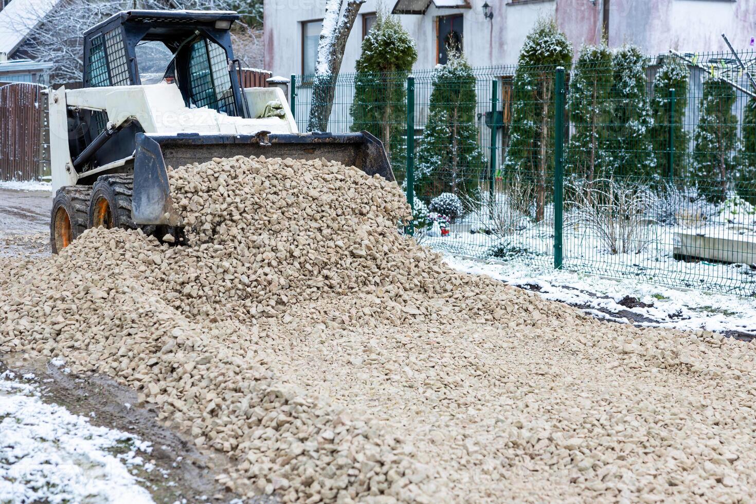 Loader Spreading Gravel on Snow Dusted Pathway Near Residential Area photo