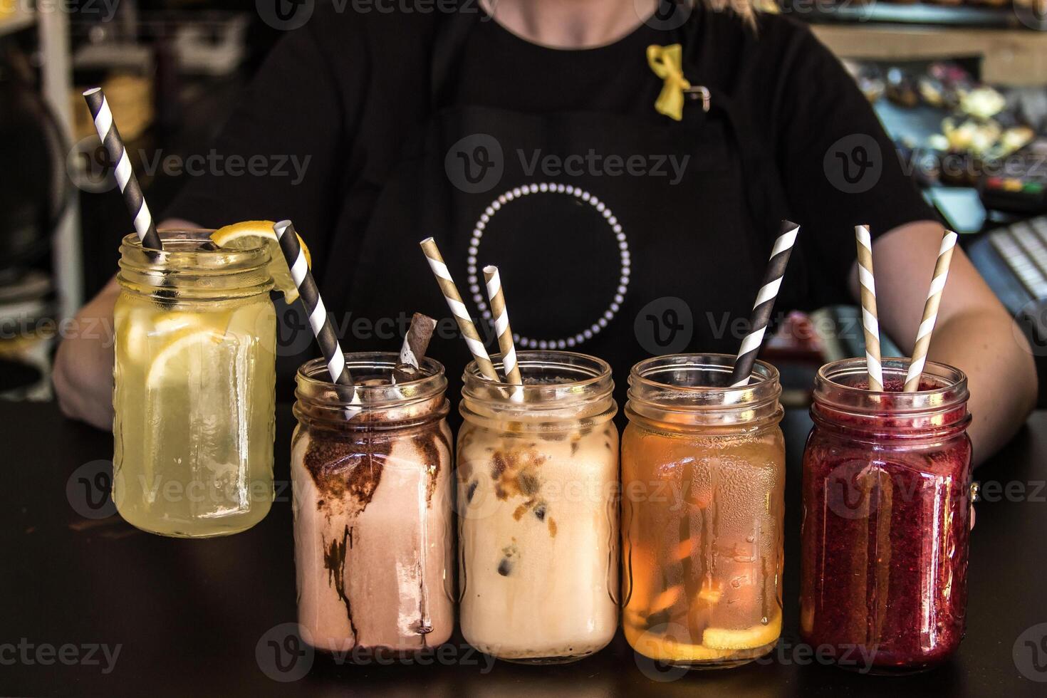 Person in Black Apron with Drinks Displayed in Mason Jars at Cafe photo
