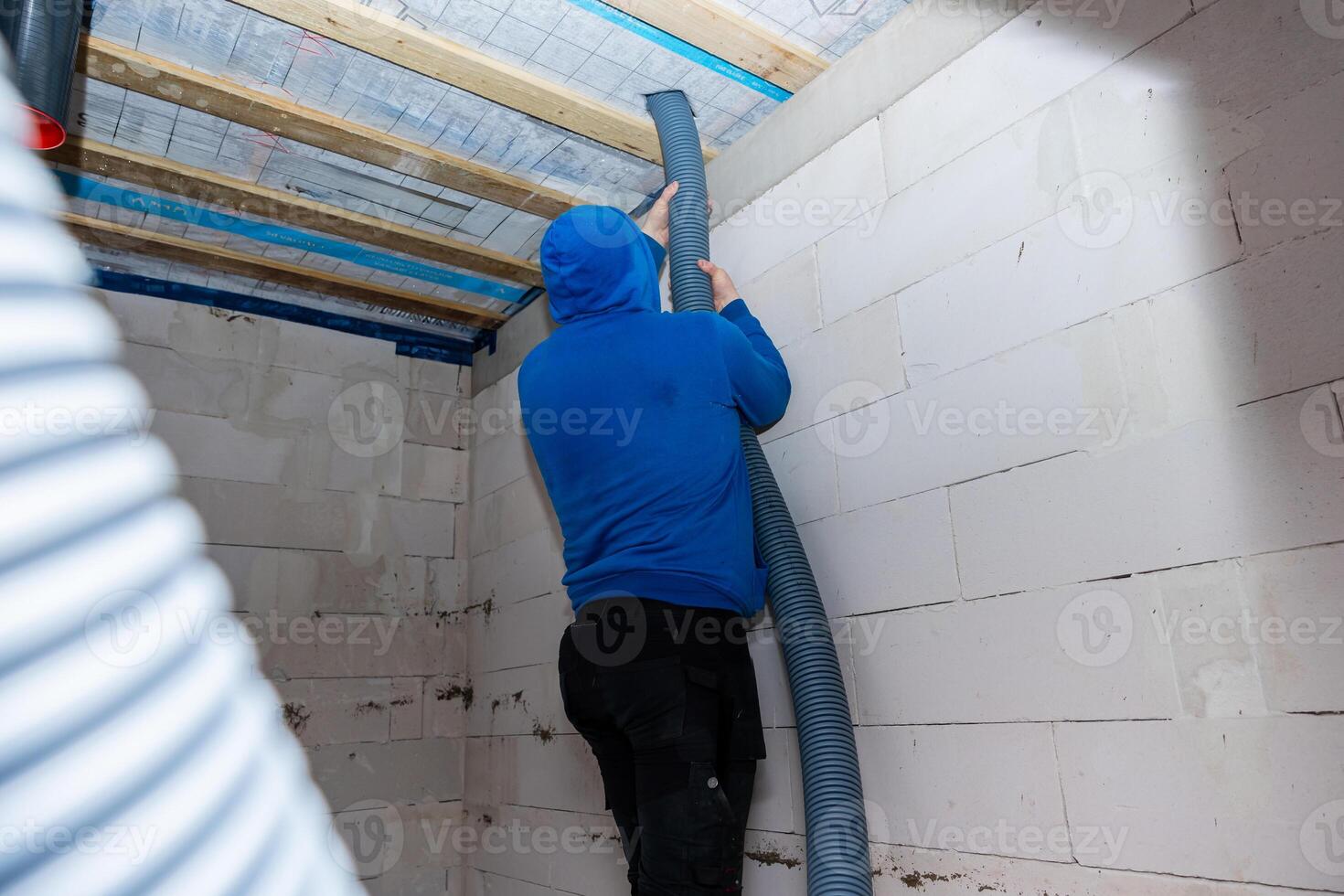 Person Installing Ventilation Duct in Room with Exposed Wooden Beams photo