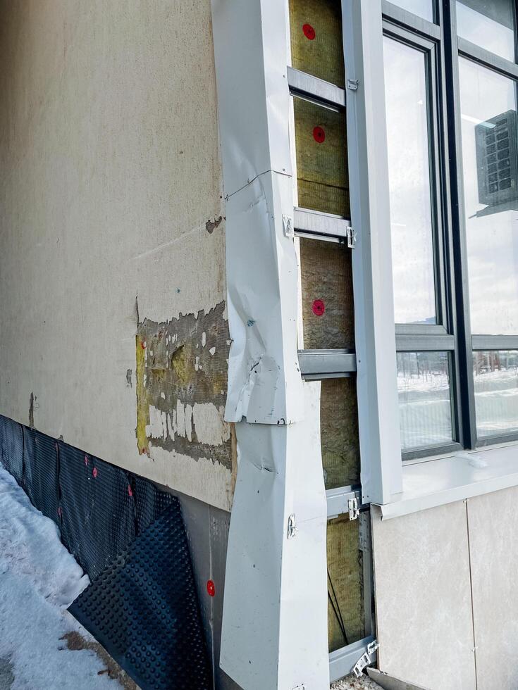 There is noticeable exterior damage on the wall of the building located near a window, which has resulted in insulation being exposed and visible to the outside elements photo