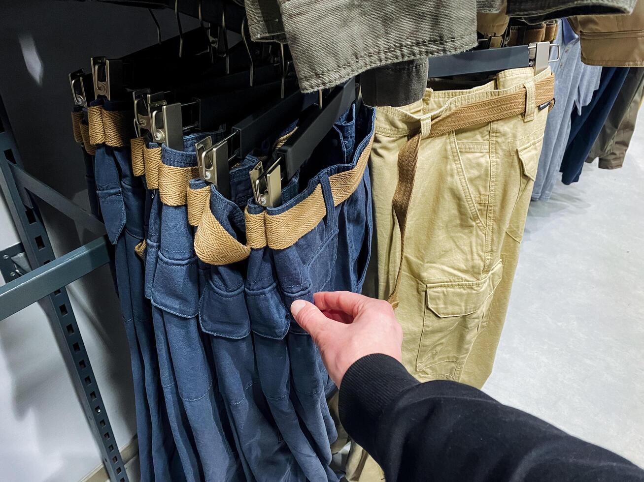 A person is currently in a clothing store selecting a stylish pair of pants, examining various options available, which may include denim fabrics and functional details like pockets photo