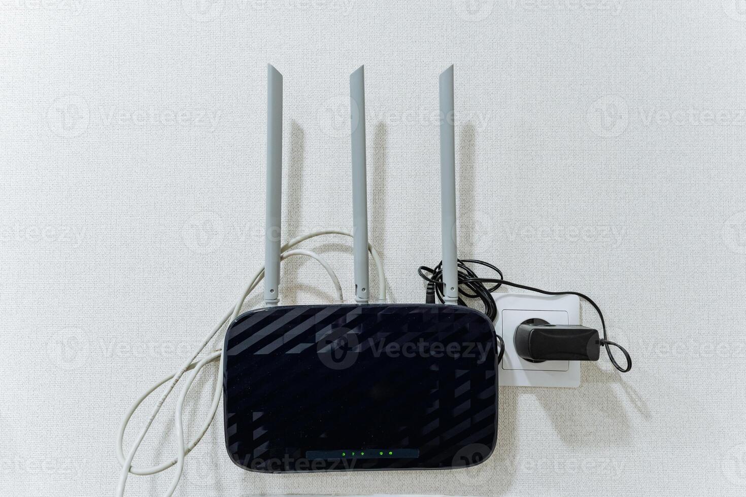A wireless router is placed on a clean white wall right next to an electrical charger, which is also an essential electronic device for powering various gadgets and technology photo