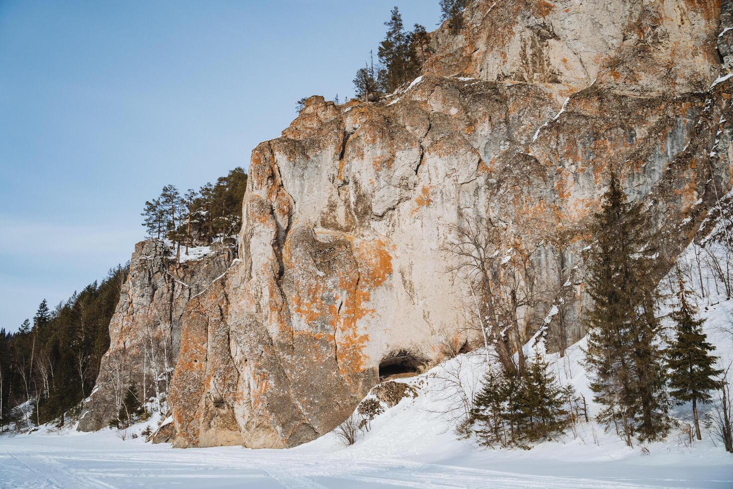 The snowcovered rock formation has inviting entrances, surrounded by tall evergreens, creating a serene winter landscape that evokes tranquility and adventure photo