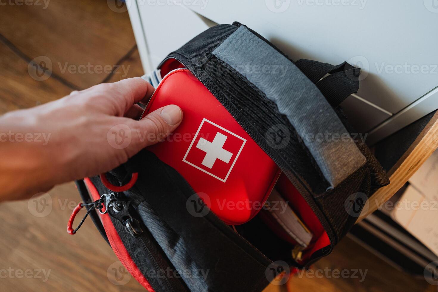 This stock photo captures a hand reaching out for a first aid kit that is tucked away inside a backpack, embodying themes of wellness, preparedness, and medicinal care
