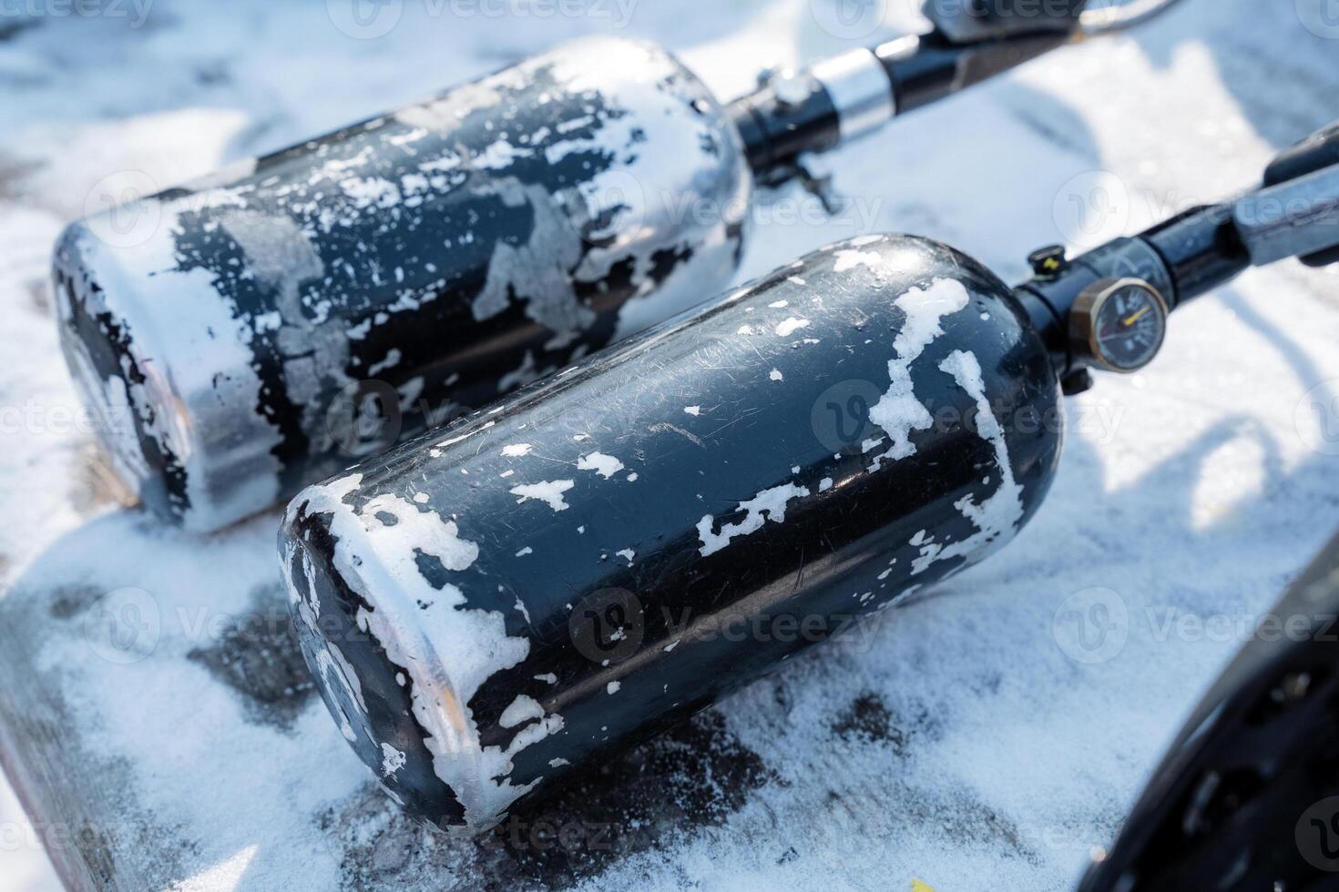 Two gas bottles are positioned and resting on a surface that is completely covered in snow, showcasing the cold winter environment surrounding them with its icy conditions photo