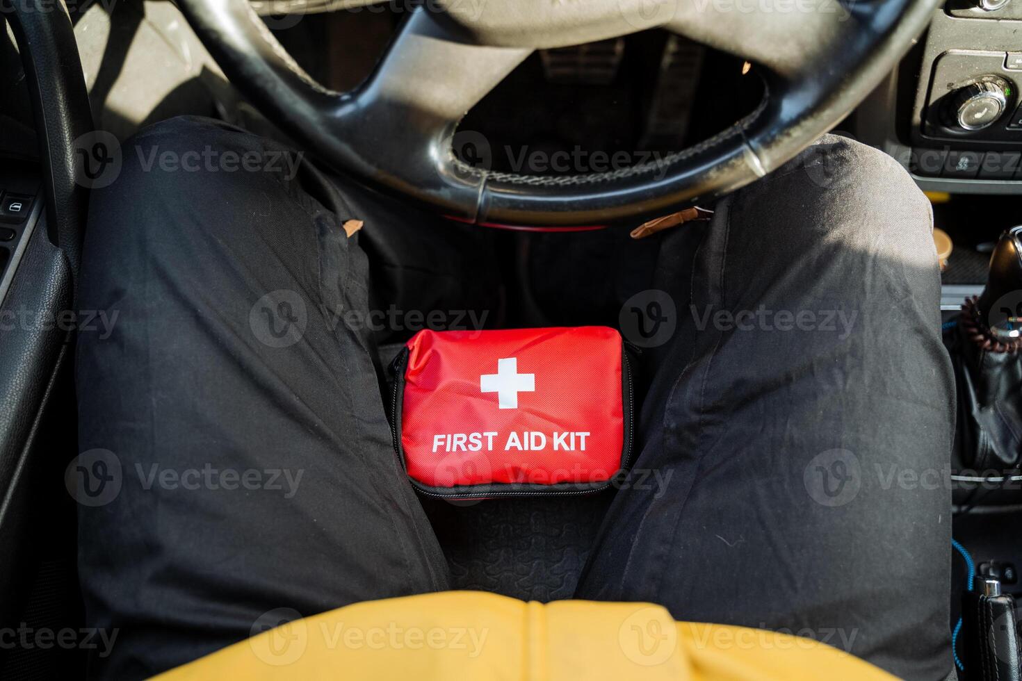A person is seated comfortably in the drivers seat of their car, with a fully stocked first aid kit placed on their lap, prepared for any potential emergencies that may arise while driving photo