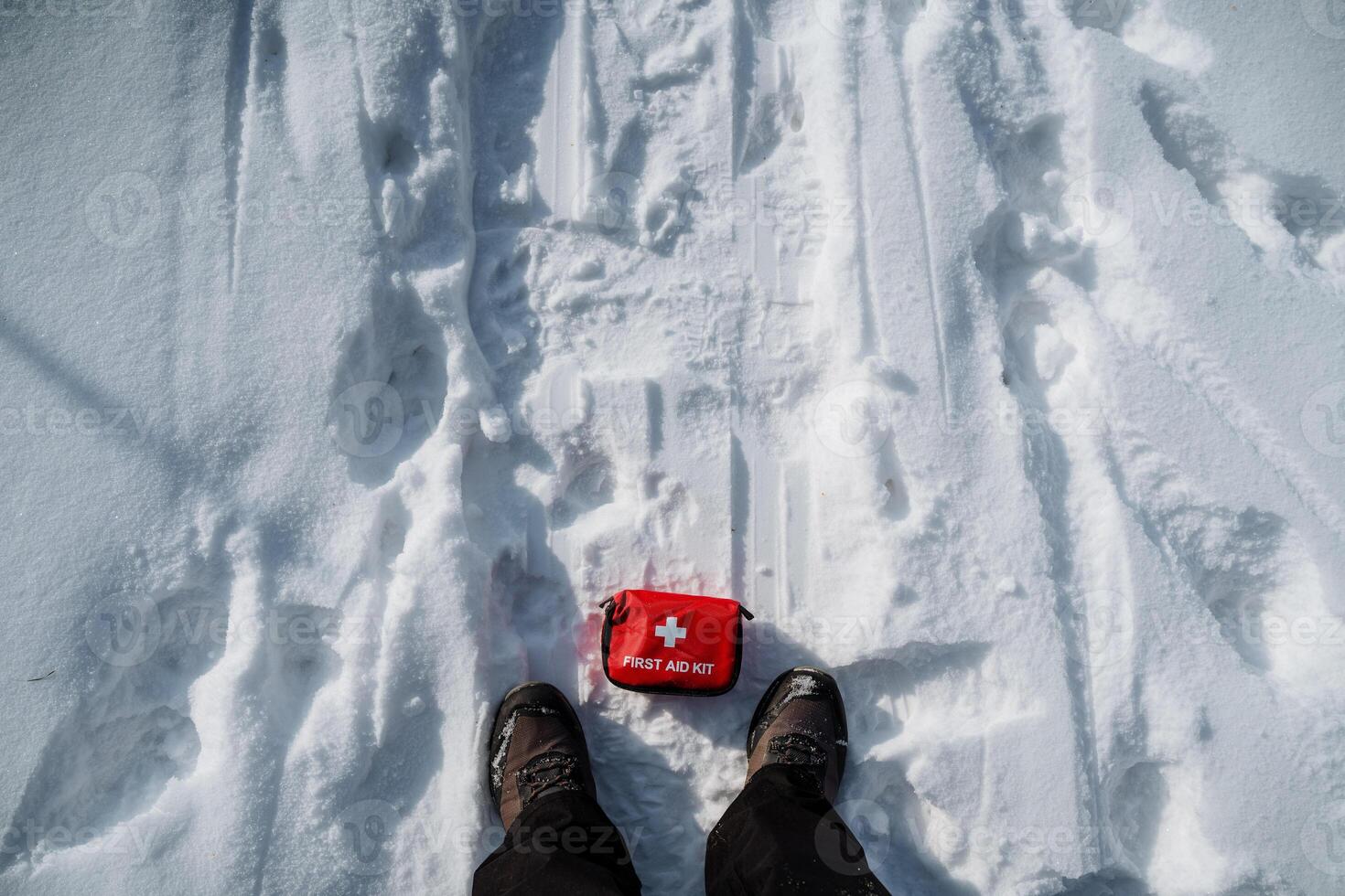 A person is standing in the fresh snow, with a first aid kit carefully placed on the ground beside them, ready for any possible injuries that may occur while enjoying the winter outdoors photo