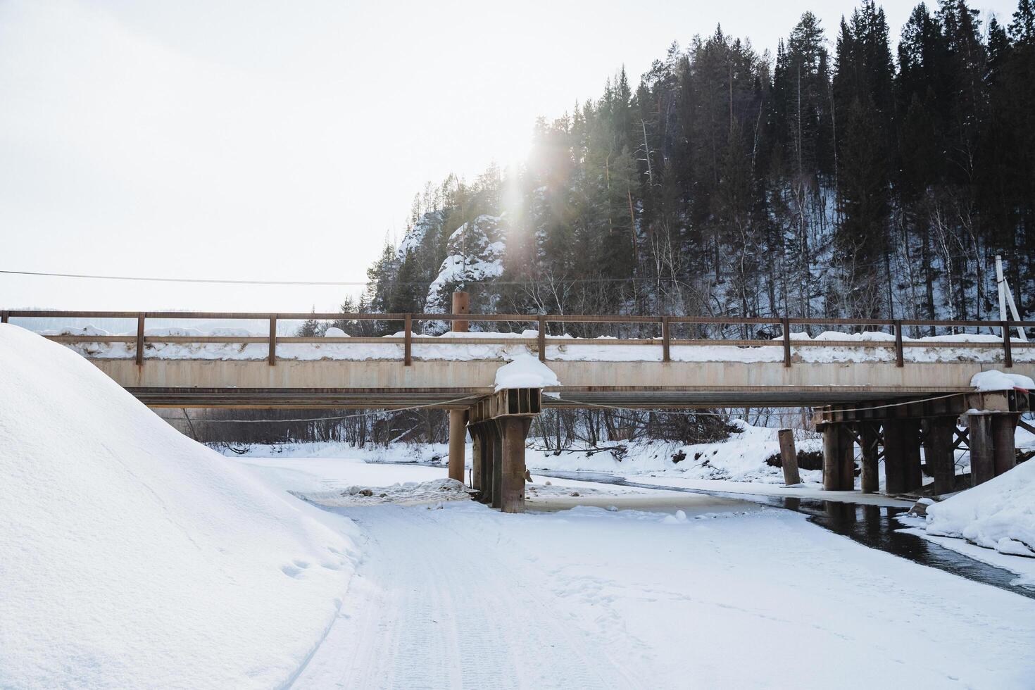A charming bridge gracefully spans a tranquil river that is elegantly dusted with pristine white snow, showcasing natures icy beauty during the serene and peaceful winter season photo