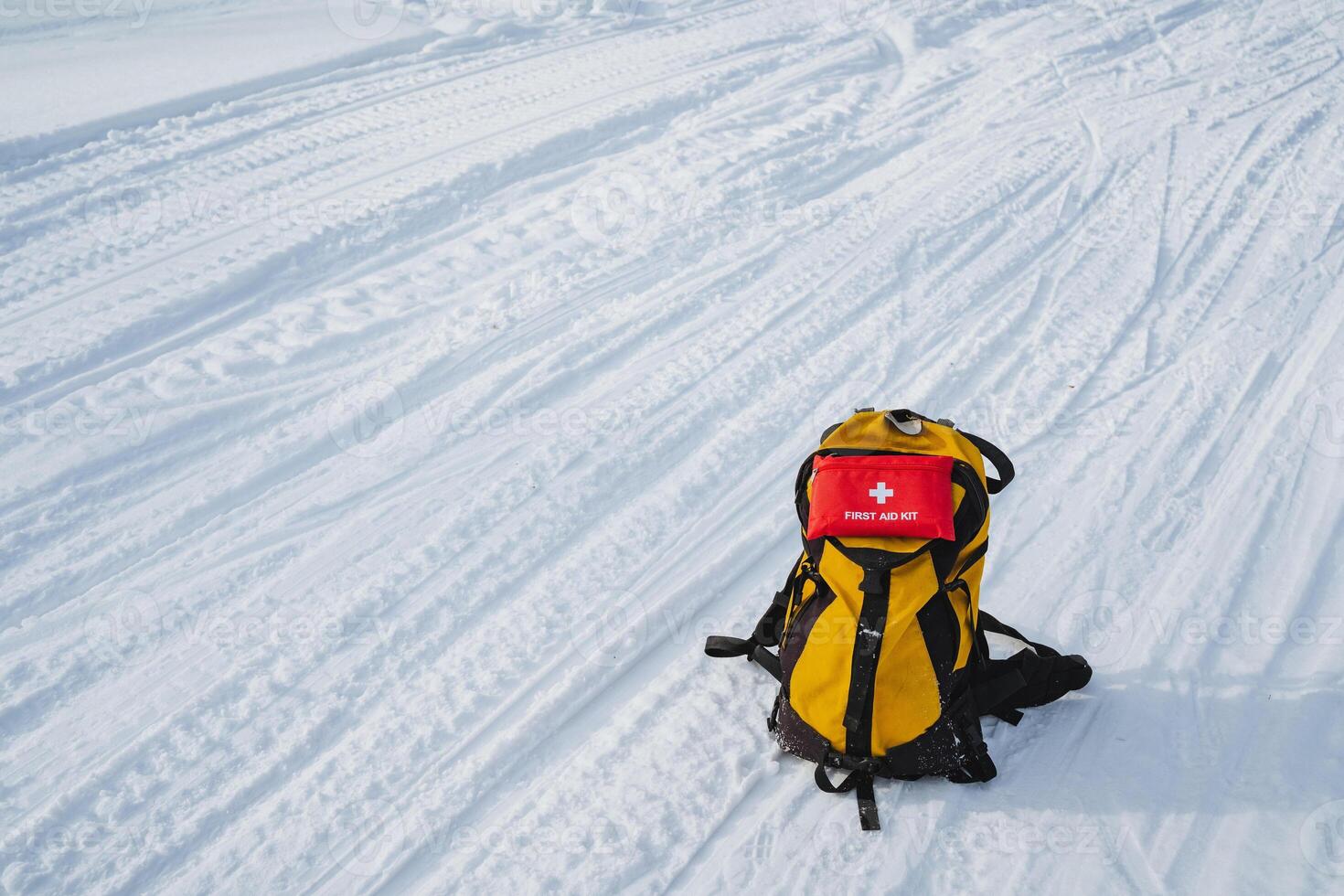 A bright yellow backpack sits prominently in the snow, accompanied by a striking red first aid kit, highlighting the adventure and preparations needed for winter activities photo