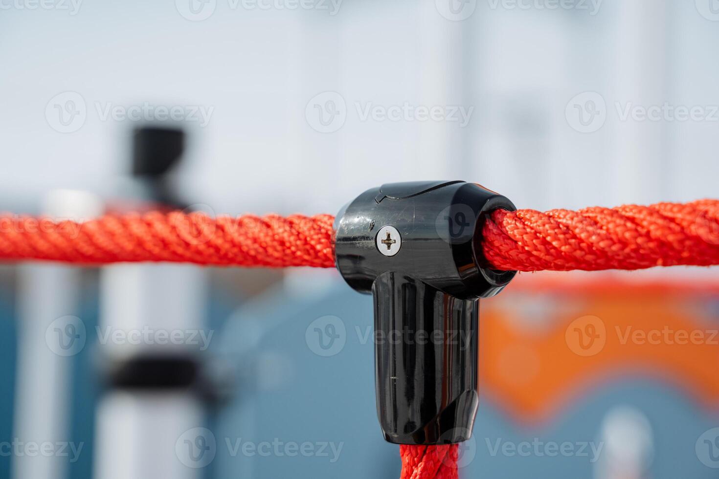 This image shows a closeup of a vibrant black and orange rope connector in a lively outdoor setting with playground equipment, capturing active recreation and joy photo