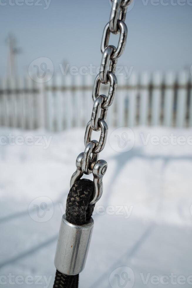 A closeup of a heavyduty metal chain attached to a sturdy rope, set against a winter landscape that showcases the seasons charm and invites appreciation for the outdoors photo