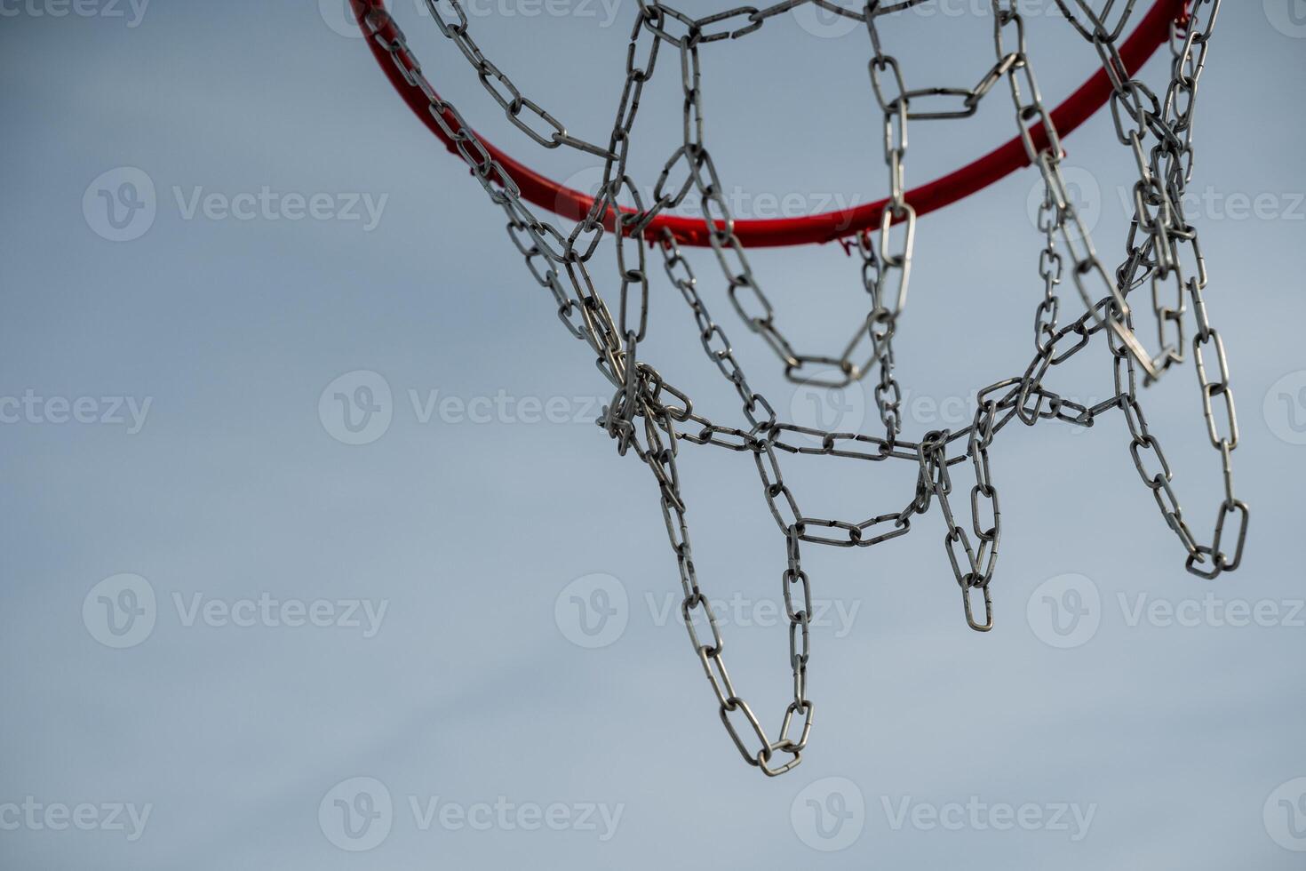 This detailed closeup image of a basketball hoop, featuring a shiny chain net contrasted against a vibrant blue sky, greatly enhances its overall visual appeal and attraction photo