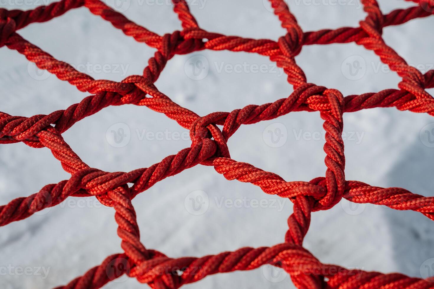 This is a closeup view of a vibrant red climbing net, complete with knots, situated on a playground surface designed for childrens adventures and safe exploration activities photo