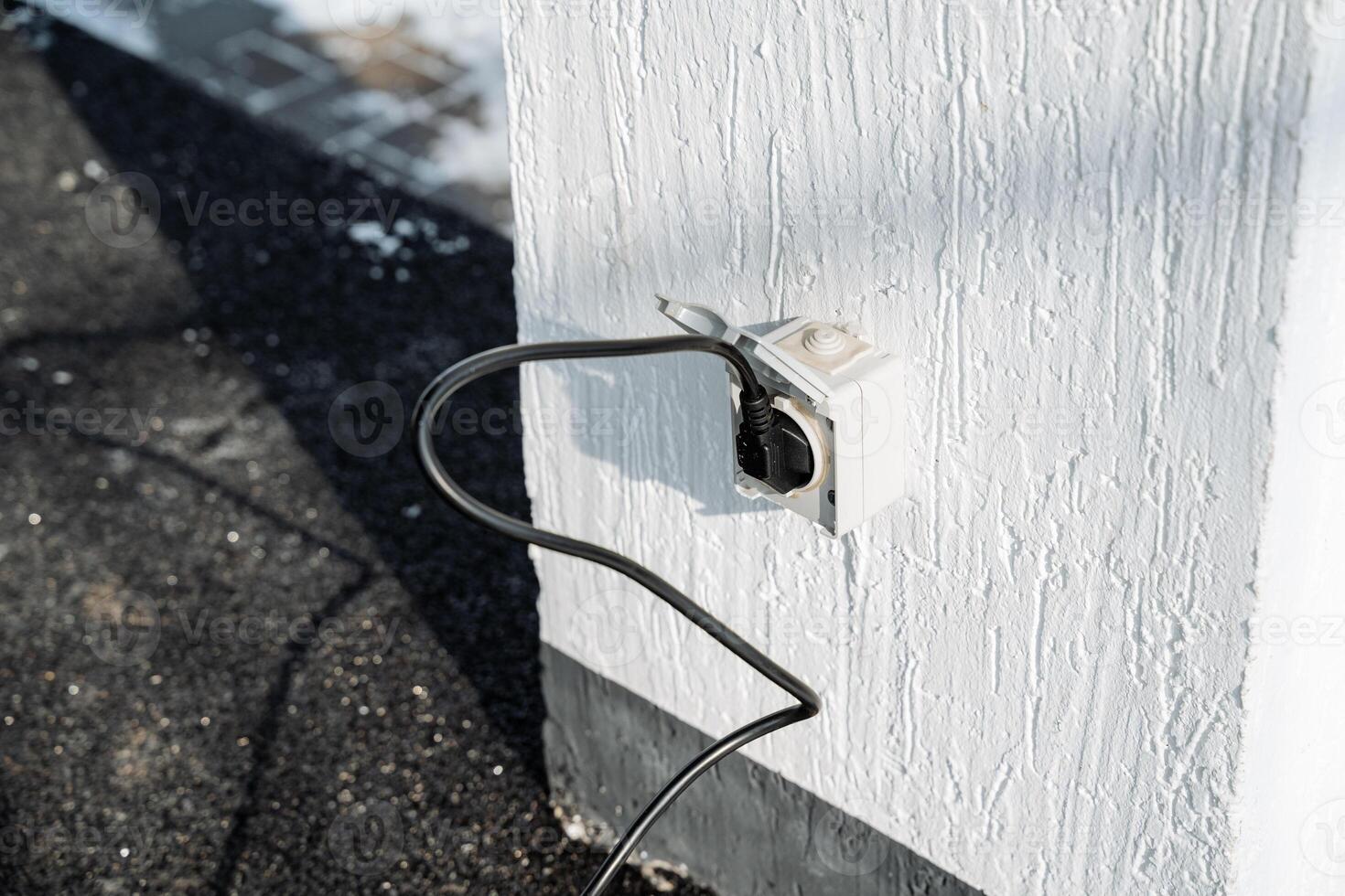 An Outdoor Electrical Outlet featuring a Plugged Power Cord mounted on a Wall, serving as a vital component for various outdoor electrical needs and functionalities photo