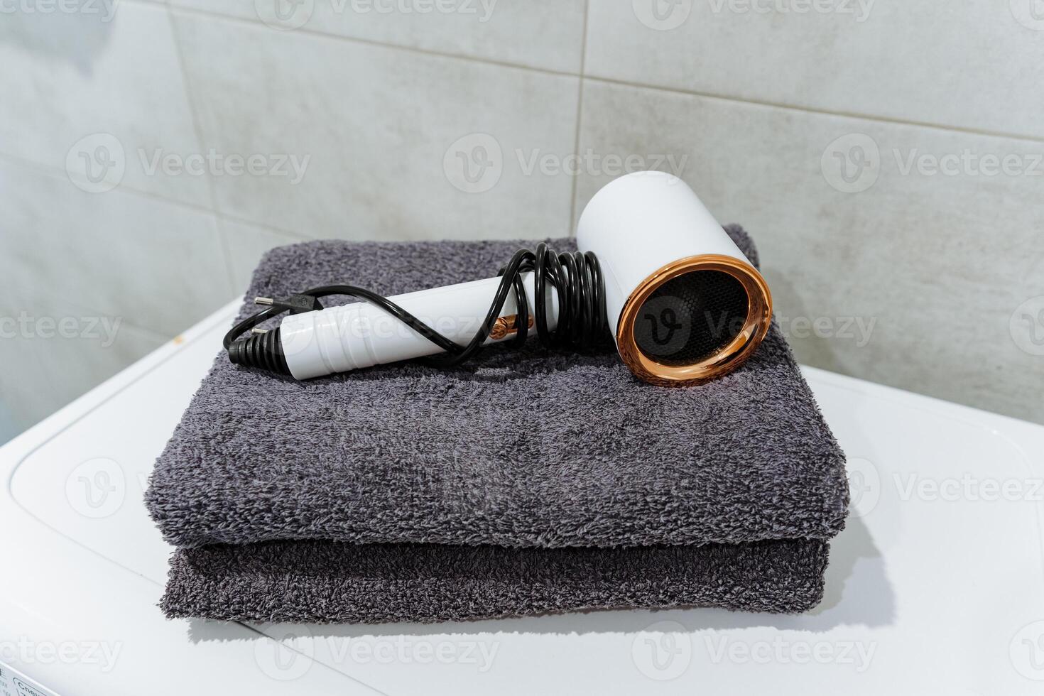 At this moment, a hair dryer is resting atop a neatly arranged stack of fluffy towels, ready to be used for personal grooming or beauty routines in a cozy bathroom setting photo