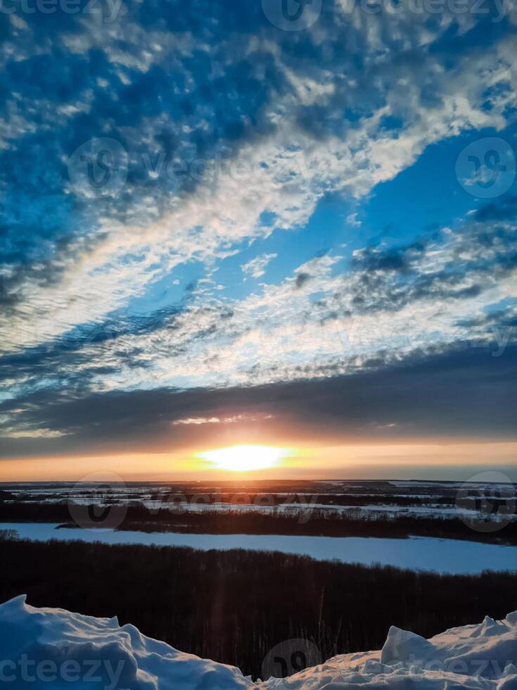 As the day comes to a close, the sun is gracefully setting over a pristine, snowy landscape, painting the sky with beautiful hues of orange and pink, creating a serene winter scene photo