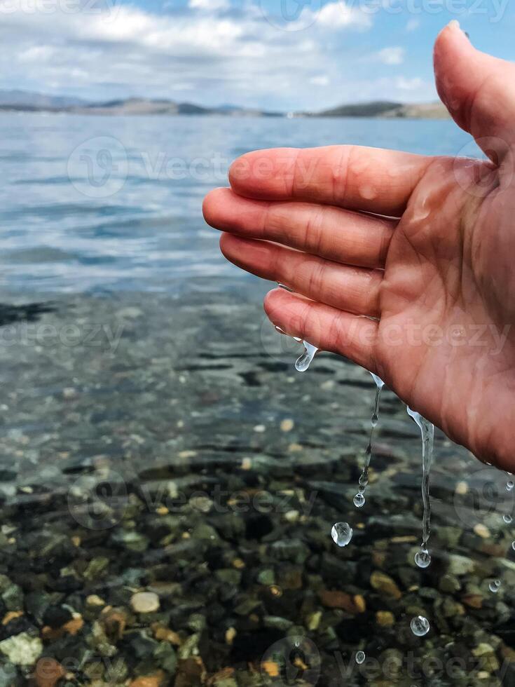 A hand is gently reaching out toward the calm surface of a lovely body of water, inviting a connection with the soothing element, as nature surrounds the scene beautifully photo