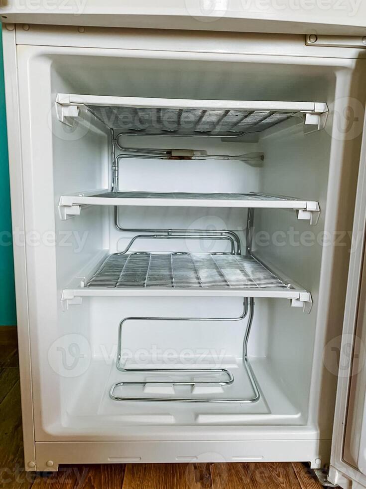 The interior space of a completely empty refrigerator is prominently visible, with the appliances door standing wide open, revealing only its vacant shelves and compartments located inside photo