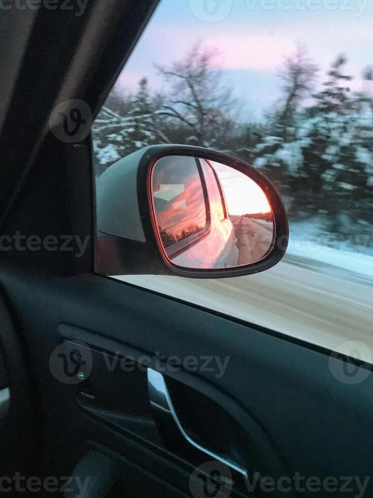 A car skillfully maneuvers along a slippery snowy road while a breathtakingly stunning sunset casts its warm, golden light over the calm and peaceful winter landscape all around photo