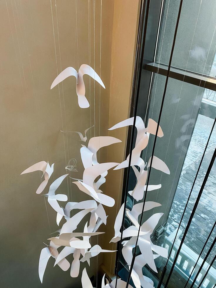 A colorful bunch of delicate paper birds is gracefully hanging from a thin string right in front of a window, creating a beautiful and whimsical display of art and design photo