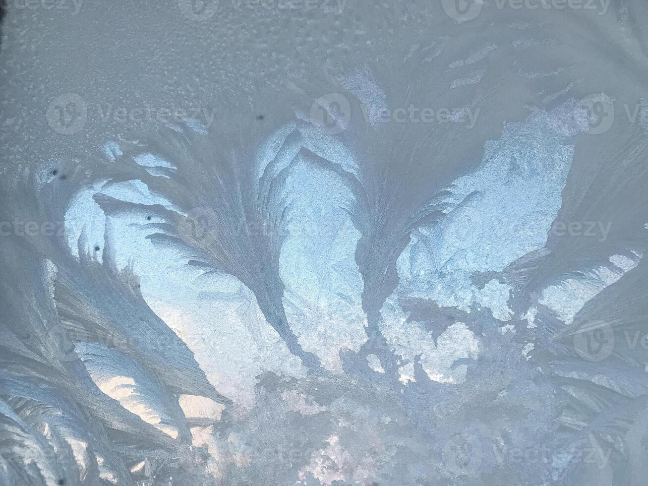 This stunning image features a closeup of intricate frost on a window, beautifully contrasting against an infinite clear blue sky, creating a mesmerizing visual experience photo