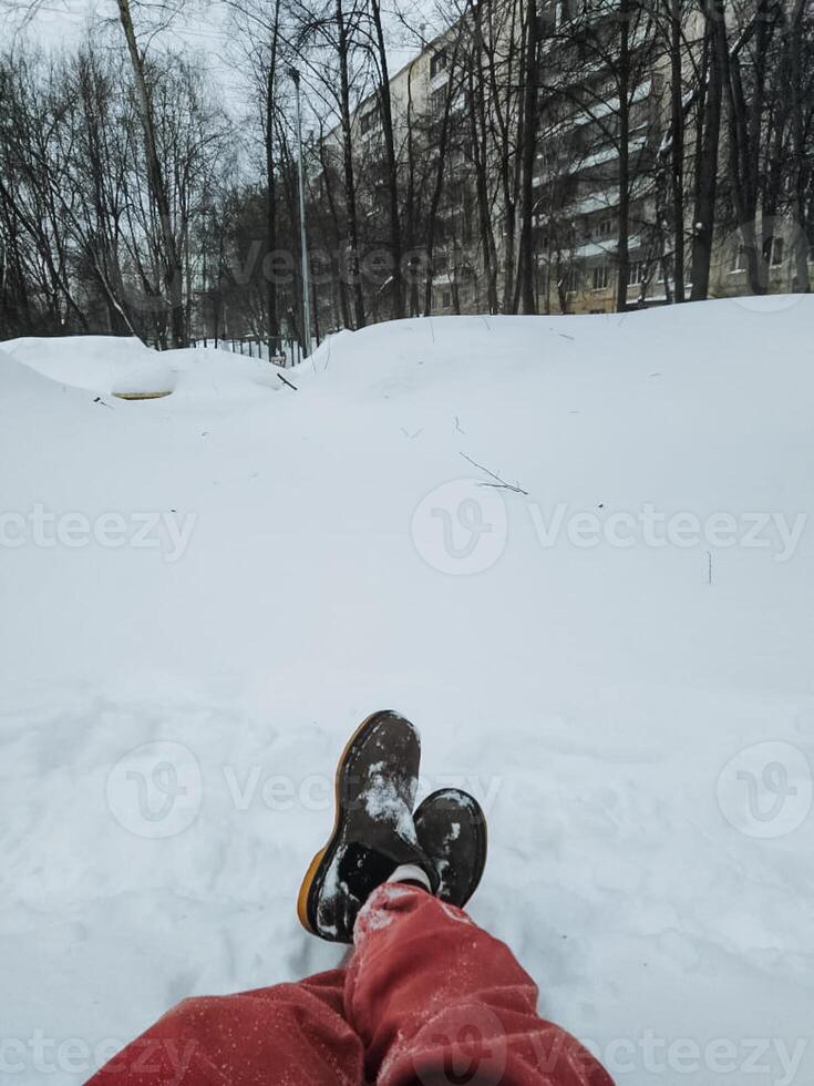A person is currently lying comfortably in the soft, white snow with their feet raised high up into the air, taking in and thoroughly enjoying the cold and wintry weather surrounding them photo