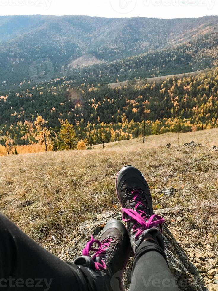 A person is comfortably relaxed on a large rock, with their feet propped up, enjoying and taking in the breathtaking view of a stunning mountain range that stretches far into the background photo