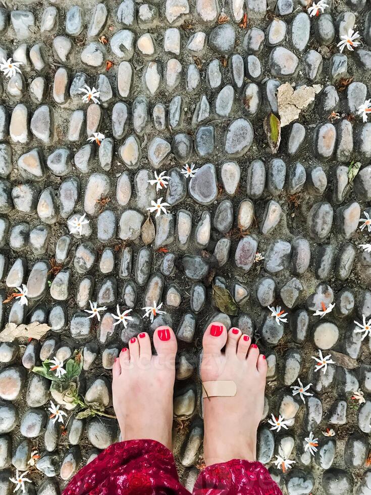 A persons feet, beautifully adorned with bright red nail polish, are standing steadily on a cobblestone stone walkway, showcasing a stylish blend of elegance and casual comfort photo
