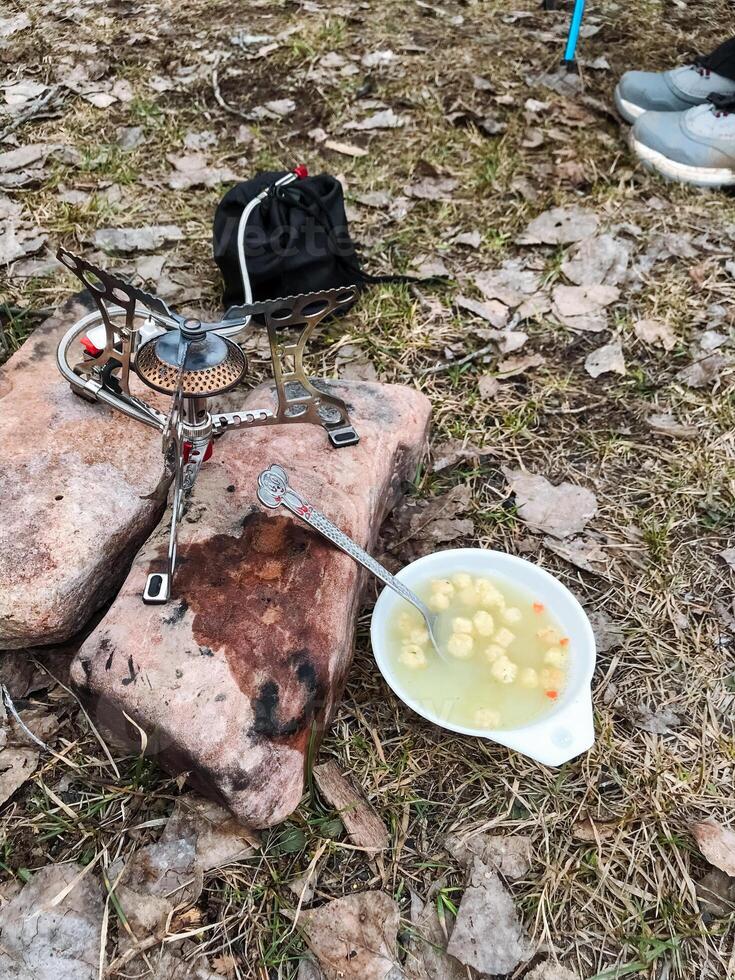 A beautifully crafted bowl filled with warm, delicious soup is resting on a large rock, which is conveniently located right beside a stove that is actively being used for cooking photo