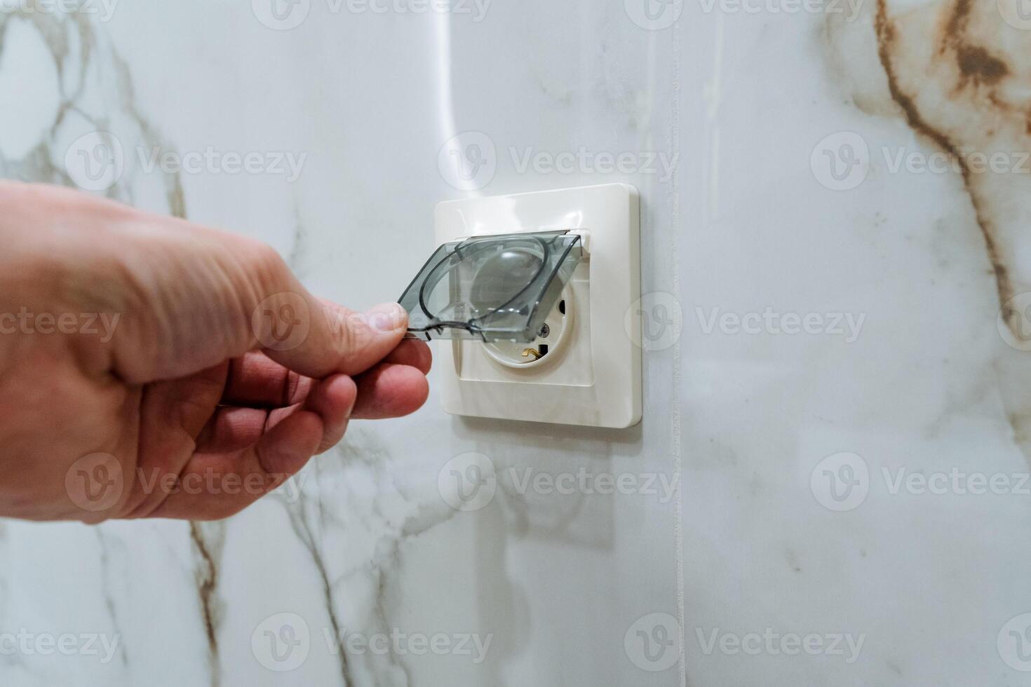 Carefully Hand Plugging a Modern Plugging Device into a Stylish Wall Socket Set Against an Elegant Marble Background for a Contemporary and Comfortable Indoor Lifestyle photo