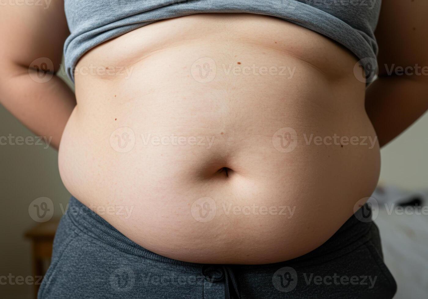 A person's midsection is slightly overweight with gray clothes on in a close up. photo