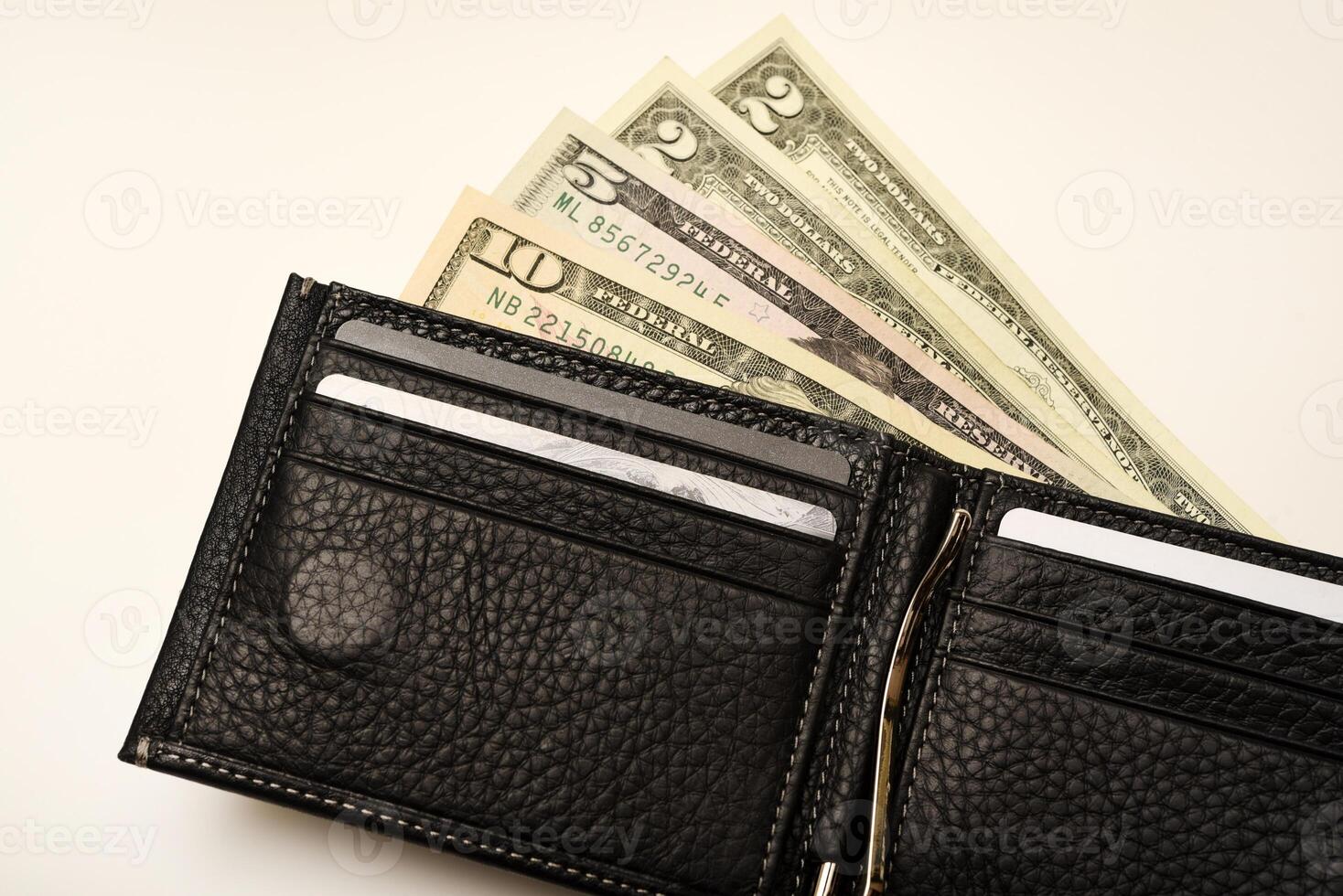 A raven-colored billfold with dollars resting on a white setting. photo