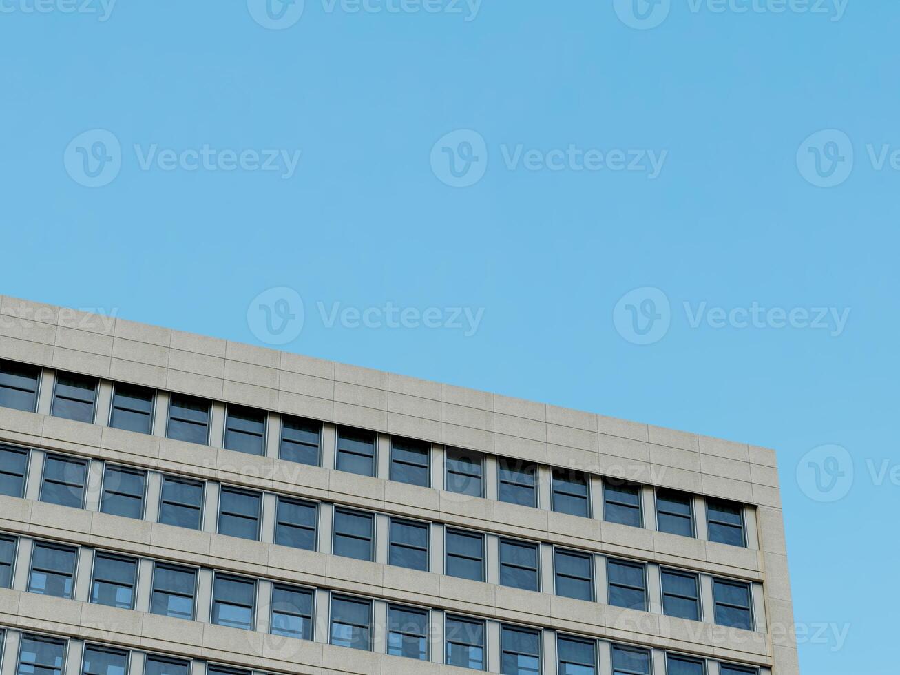 Modern skyscraper corner with geometric stone and glass design, under a bright blue sky. photo