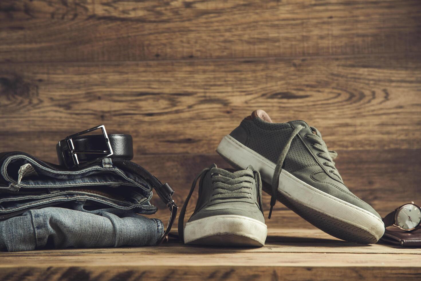A pair of sneakers, jeans, belt and shoes on a wooden table photo