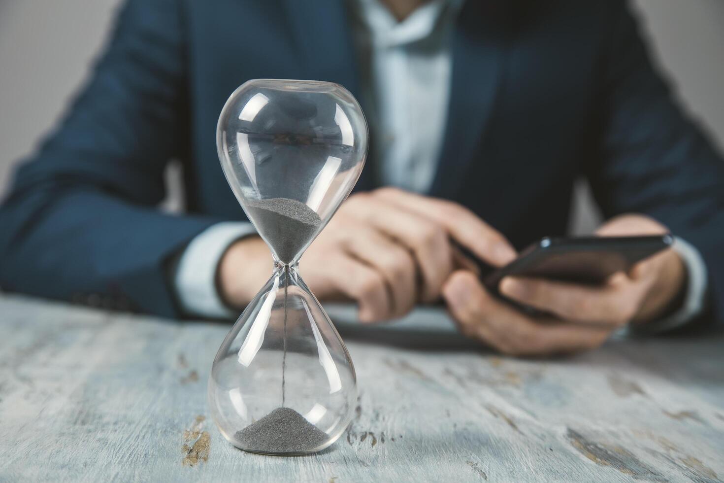 A man in a suit is using his phone while holding an hourglass photo