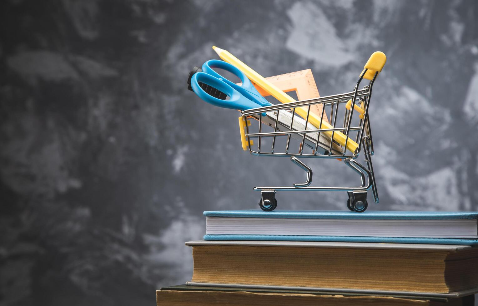 A shopping cart with scissors and books on top of a stack of books photo